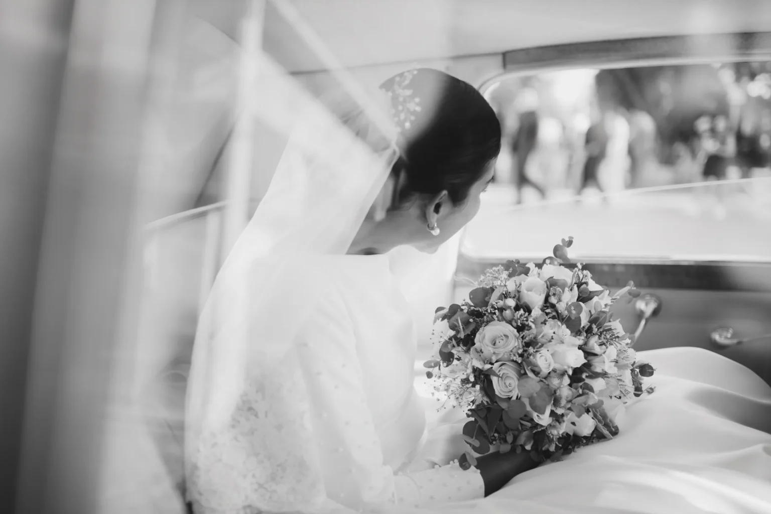 A cinematic black and white shot of a bride with a bouquet in a vintage car, Mexico Destination Wedding Photography by Poga Studios